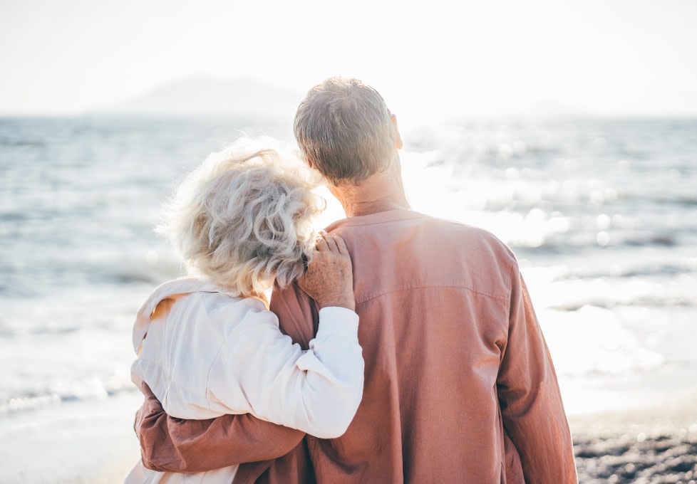 Middle aged couple stood with their arms around each other watching the ocean